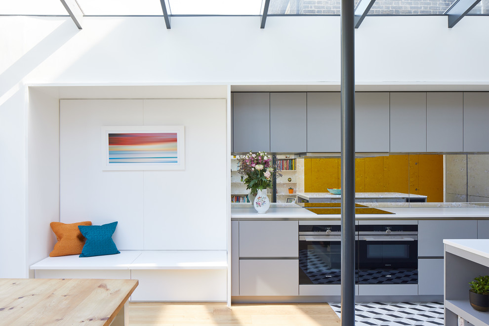 Moderne Wohnküche mit flächenbündigen Schrankfronten, grauen Schränken, Rückwand aus Spiegelfliesen, Kücheninsel, buntem Boden und weißer Arbeitsplatte in London