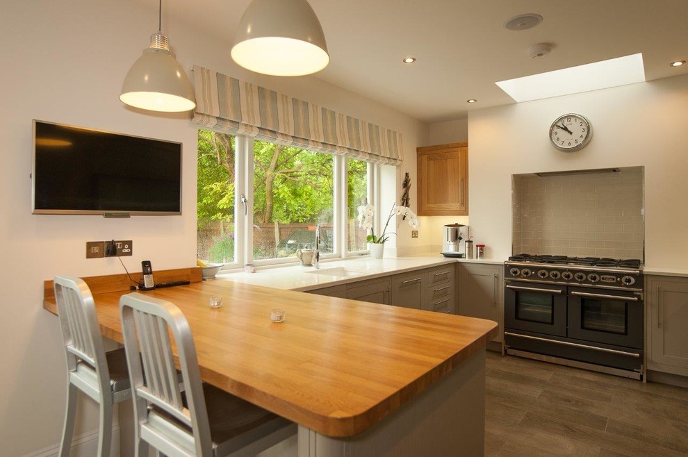 This is an example of a medium sized contemporary u-shaped kitchen/diner in Hertfordshire with a belfast sink, shaker cabinets, beige cabinets, granite worktops, beige splashback, mosaic tiled splashback, stainless steel appliances, light hardwood flooring, a breakfast bar and beige floors.