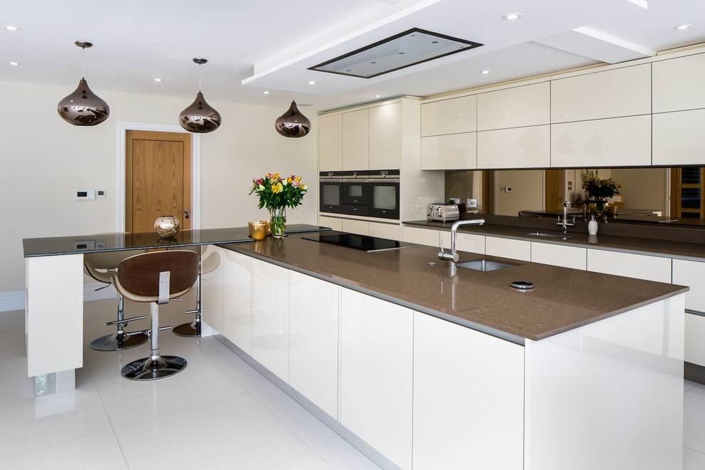 Inspiration for a large contemporary galley kitchen in Hertfordshire with flat-panel cabinets, metallic splashback, mirror splashback, stainless steel appliances, slate flooring, brown worktops, a submerged sink, beige cabinets, an island and white floors.