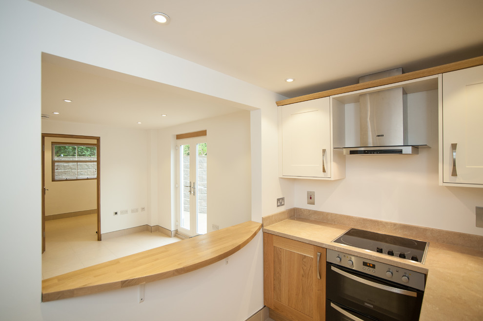 Small contemporary galley kitchen/diner in Hertfordshire with a built-in sink, raised-panel cabinets, medium wood cabinets, marble worktops, beige splashback, slate splashback, stainless steel appliances, ceramic flooring, a breakfast bar and beige floors.