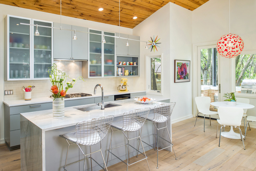 1960s galley light wood floor open concept kitchen photo in Austin with an undermount sink, flat-panel cabinets, gray cabinets, quartzite countertops, gray backsplash, ceramic backsplash, stainless steel appliances and an island