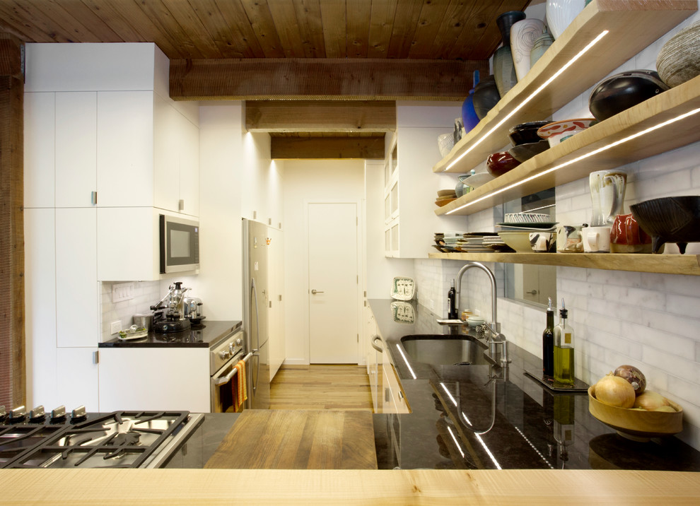Bild på ett mellanstort eklektiskt kök, med en undermonterad diskho, släta luckor, vita skåp, träbänkskiva, vitt stänkskydd, stänkskydd i stenkakel, rostfria vitvaror, mörkt trägolv och en halv köksö