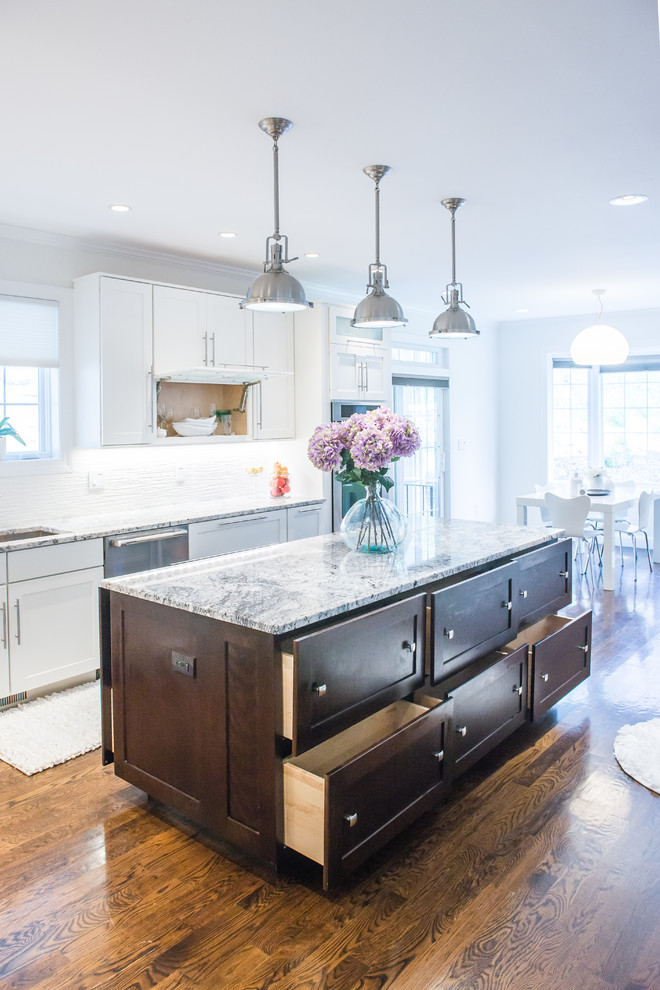 Inspiration for a mid-sized transitional l-shaped medium tone wood floor eat-in kitchen remodel in New York with shaker cabinets, white cabinets, white backsplash, an island, an undermount sink, granite countertops, ceramic backsplash and stainless steel appliances