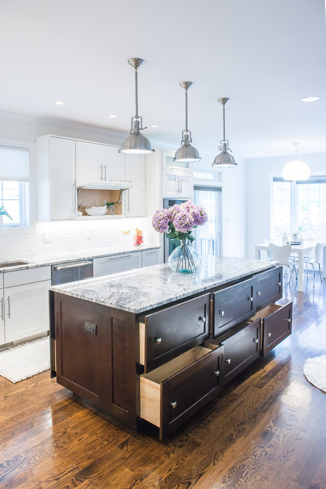 Ejemplo de cocina clásica renovada de tamaño medio con armarios estilo shaker, puertas de armario blancas, salpicadero blanco, suelo de madera en tonos medios, una isla, fregadero bajoencimera, encimera de granito, salpicadero de azulejos de cerámica y electrodomésticos de acero inoxidable