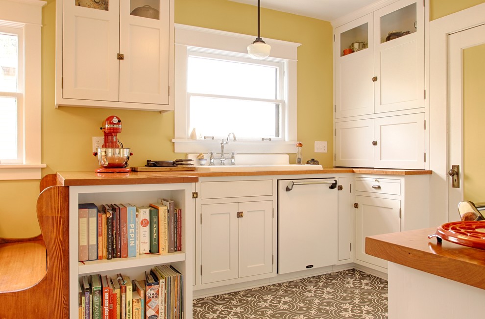 Пример оригинального дизайна: п-образная кухня в стиле кантри с обеденным столом, накладной мойкой, фасадами в стиле шейкер, белыми фасадами, деревянной столешницей, желтым фартуком, белой техникой и серым полом