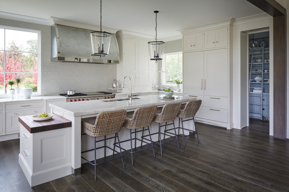 Inredning av ett klassiskt vit vitt l-kök, med en undermonterad diskho, luckor med infälld panel, vita skåp, bänkskiva i kvartsit, vitt stänkskydd, integrerade vitvaror, en köksö, mörkt trägolv och brunt golv