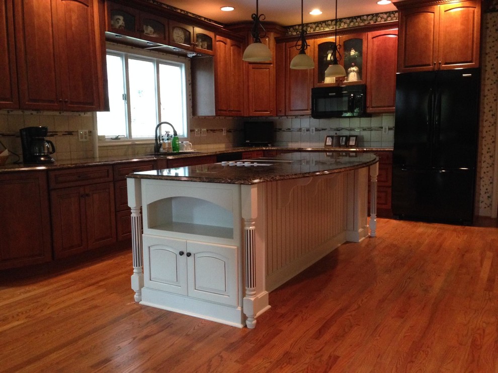 Inspiration for a large timeless medium tone wood floor eat-in kitchen remodel in Other with a double-bowl sink, raised-panel cabinets, brown cabinets, quartz countertops, beige backsplash, ceramic backsplash, black appliances and an island