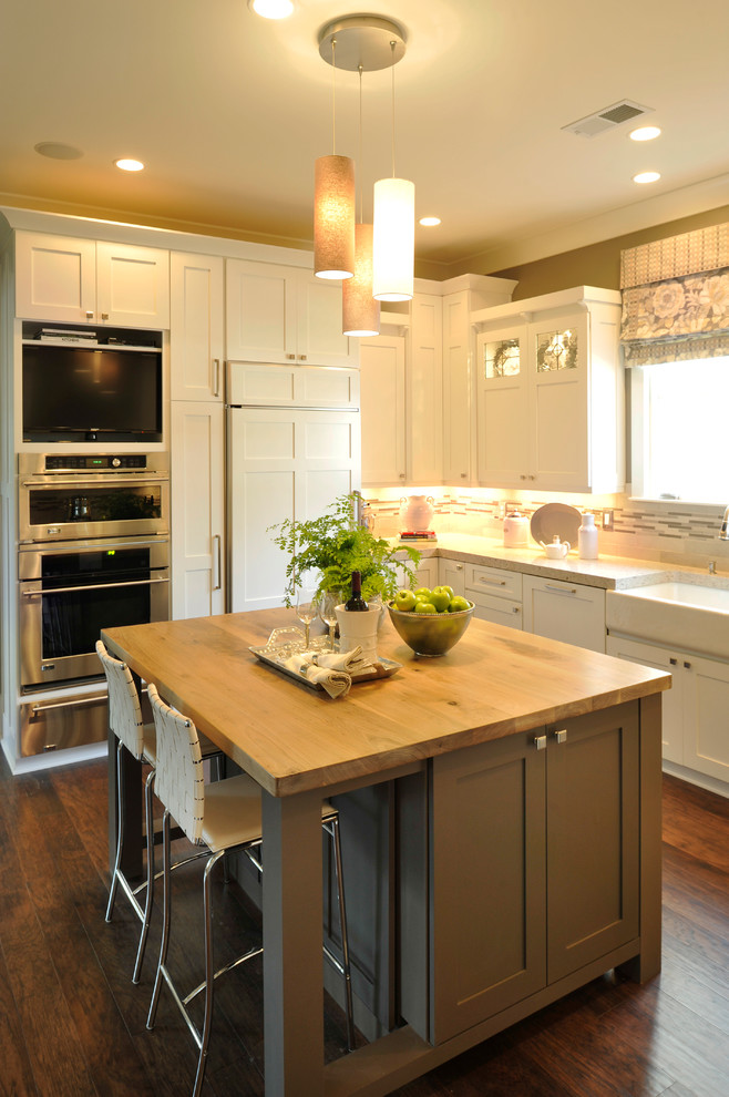 This is an example of a medium sized farmhouse grey and cream u-shaped kitchen/diner in Nashville with a belfast sink, shaker cabinets, white cabinets, granite worktops, white splashback, porcelain splashback, stainless steel appliances, dark hardwood flooring, an island and brown floors.