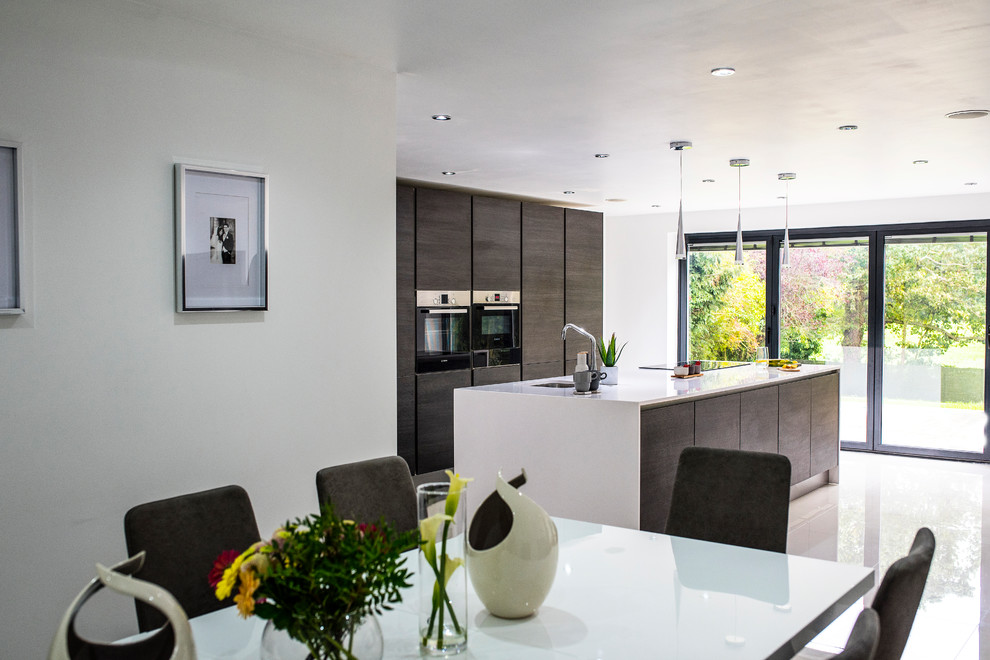 Large contemporary galley open plan kitchen in Other with a single-bowl sink, flat-panel cabinets, dark wood cabinets, quartz worktops, black appliances, porcelain flooring, an island, white floors and white worktops.