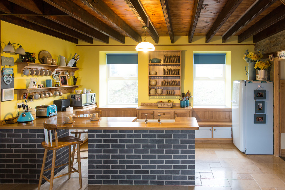 На фото: отдельная кухня в стиле кантри с с полувстраиваемой мойкой (с передним бортиком), открытыми фасадами, деревянной столешницей, желтым фартуком, белой техникой, полуостровом и бежевым полом