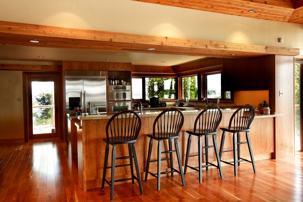 На фото: п-образная кухня-гостиная в стиле фьюжн с накладной мойкой, техникой из нержавеющей стали, коричневым полом и островом