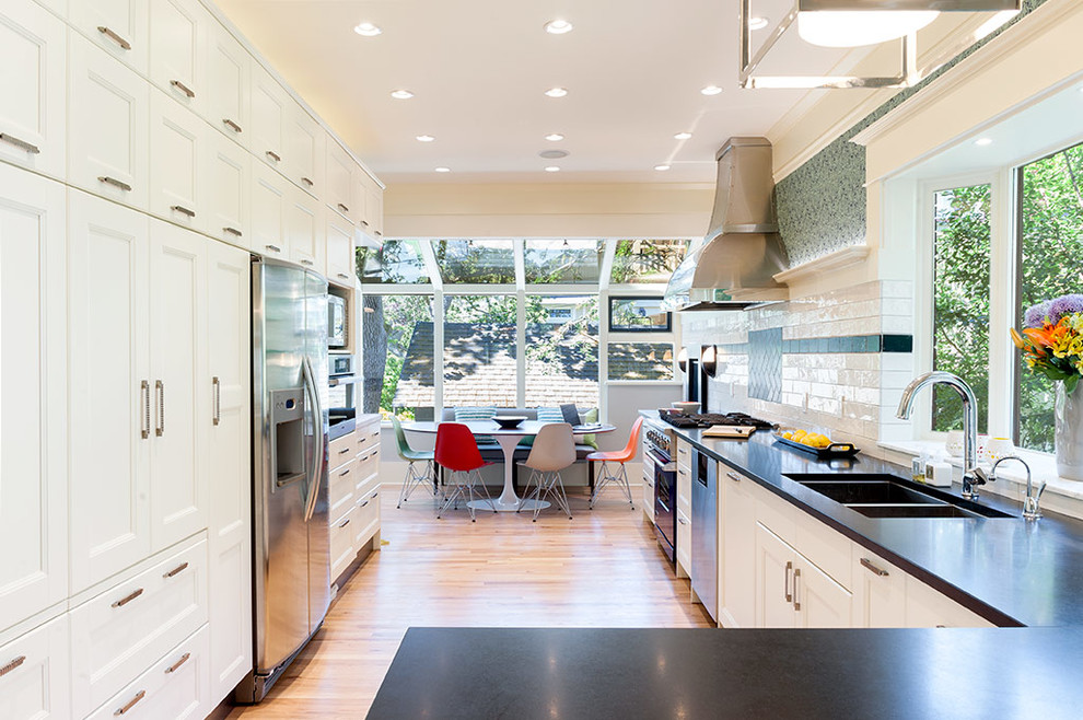 Zweizeilige, Mittelgroße Klassische Wohnküche mit Doppelwaschbecken, weißen Schränken, Granit-Arbeitsplatte, Küchenrückwand in Weiß, Rückwand aus Metrofliesen, Küchengeräten aus Edelstahl und hellem Holzboden in Vancouver