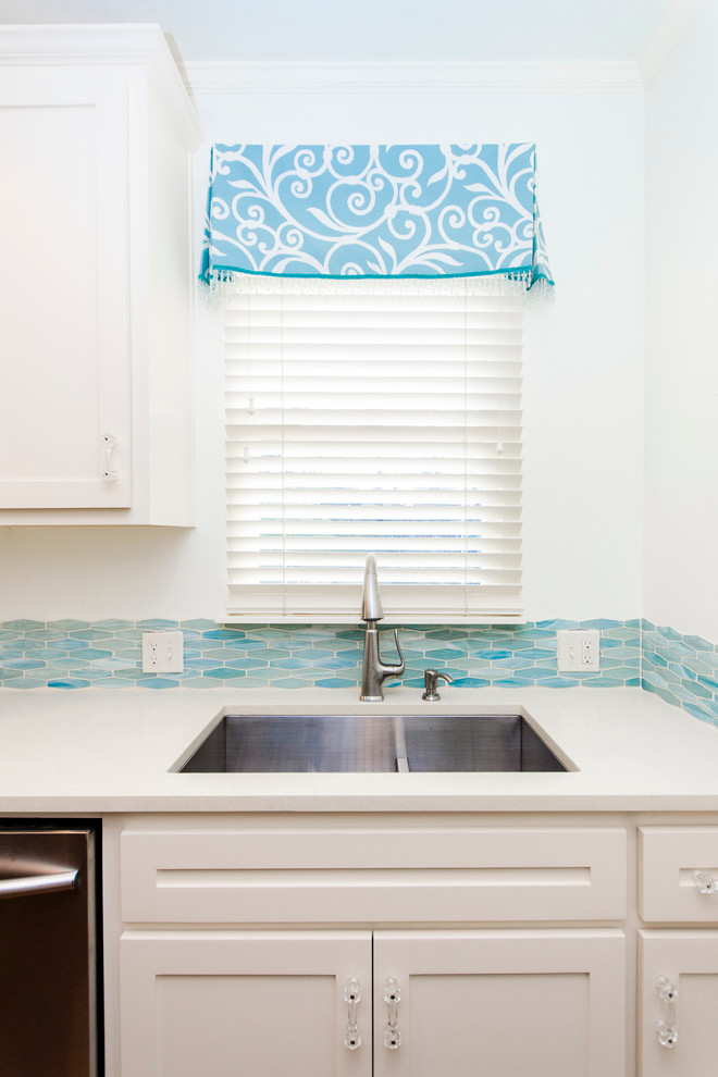 Maritim inredning av ett litet kök, med luckor med infälld panel, vita skåp, blått stänkskydd, stänkskydd i keramik, rostfria vitvaror, mellanmörkt trägolv och en undermonterad diskho