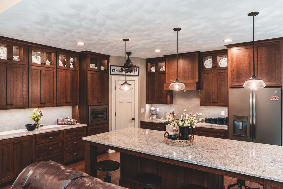 Inspiration for a large timeless u-shaped medium tone wood floor eat-in kitchen remodel in Other with a farmhouse sink, shaker cabinets, medium tone wood cabinets, quartz countertops, gray backsplash, glass tile backsplash, stainless steel appliances, an island and multicolored countertops