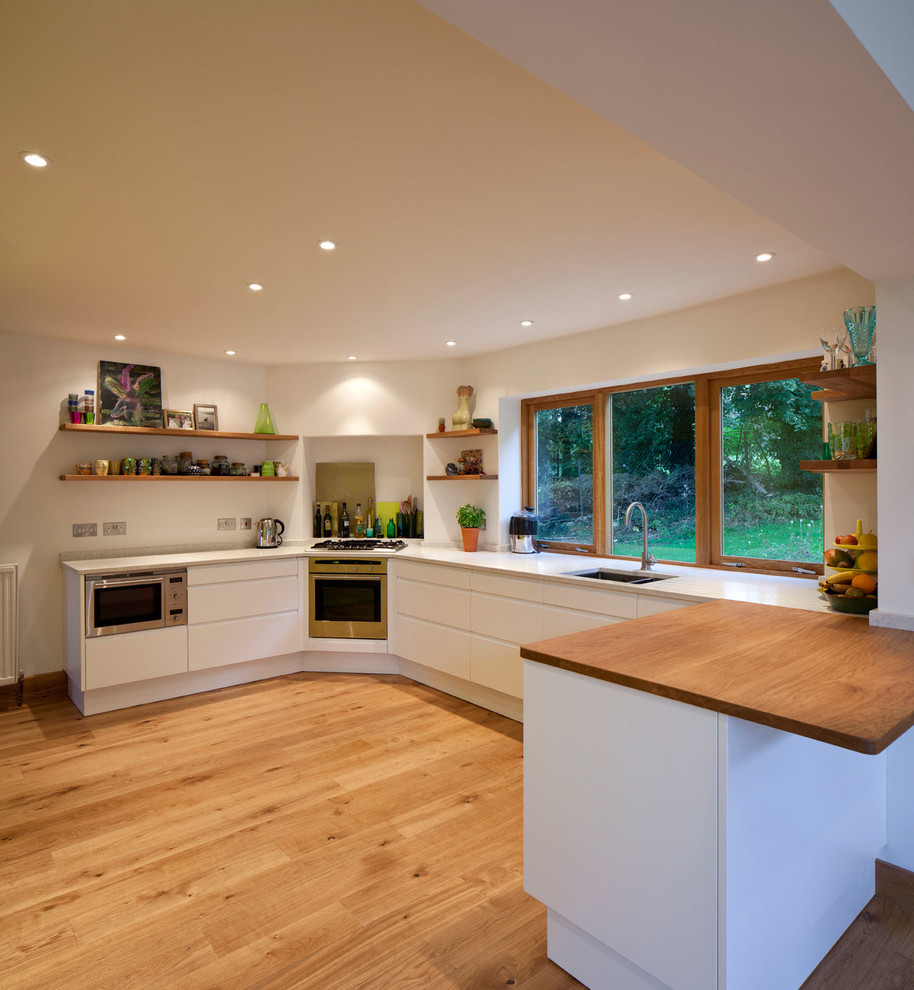 Exempel på ett modernt kök, med en undermonterad diskho, släta luckor, vita skåp, träbänkskiva och rostfria vitvaror