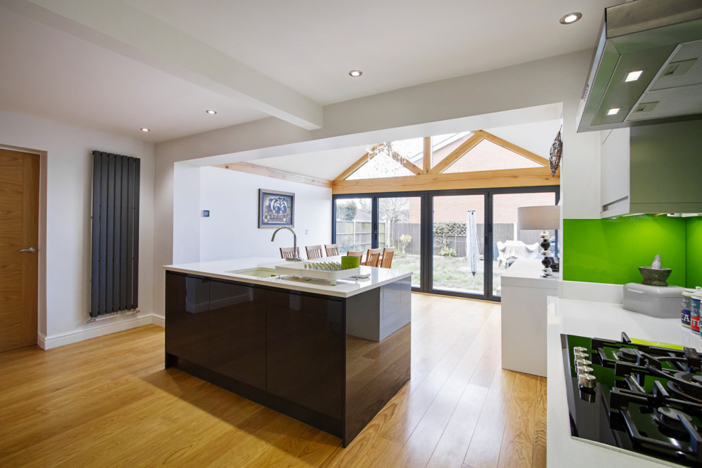 This is an example of a small contemporary l-shaped open plan kitchen in West Midlands with a built-in sink, flat-panel cabinets, grey cabinets, marble worktops, green splashback, glass sheet splashback, stainless steel appliances, laminate floors, an island, beige floors and white worktops.