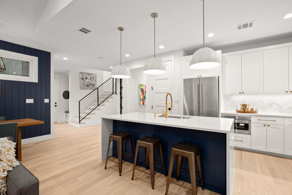 This is an example of a modern l-shaped open plan kitchen in Austin with white cabinets, white splashback, stainless steel appliances, light hardwood flooring and an island.