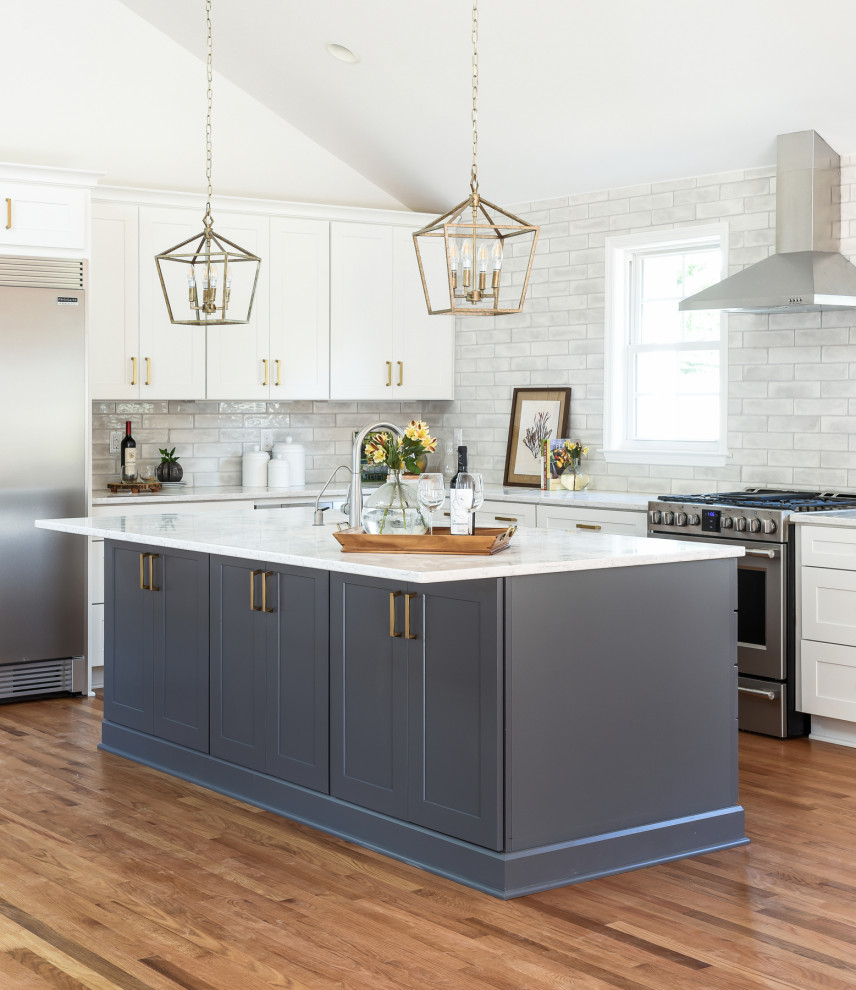 Design ideas for a large traditional l-shaped kitchen in Nashville with shaker cabinets, white cabinets, engineered stone countertops, grey splashback, metro tiled splashback, stainless steel appliances, an island, brown floors, white worktops and medium hardwood flooring.