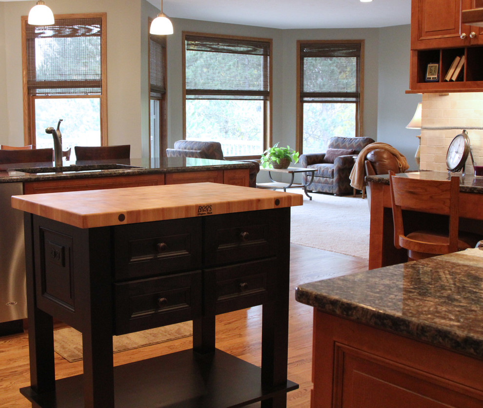 Example of a large classic l-shaped light wood floor and brown floor open concept kitchen design in Milwaukee with an undermount sink, recessed-panel cabinets, brown cabinets, granite countertops, beige backsplash, ceramic backsplash, stainless steel appliances, two islands and black countertops