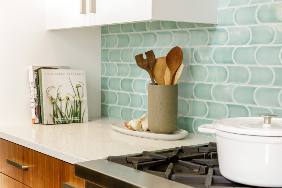 Bild på ett mellanstort 50 tals vit vitt kök, med en enkel diskho, släta luckor, skåp i mellenmörkt trä, bänkskiva i kvarts, blått stänkskydd, stänkskydd i keramik, rostfria vitvaror och mellanmörkt trägolv