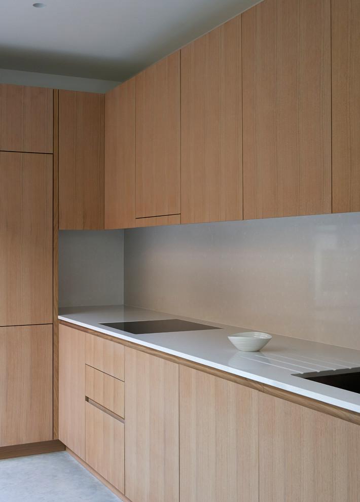 Modern inredning av ett litet kök, med släta luckor, skåp i ljust trä, bänkskiva i koppar, vitt stänkskydd, integrerade vitvaror, en integrerad diskho och betonggolv