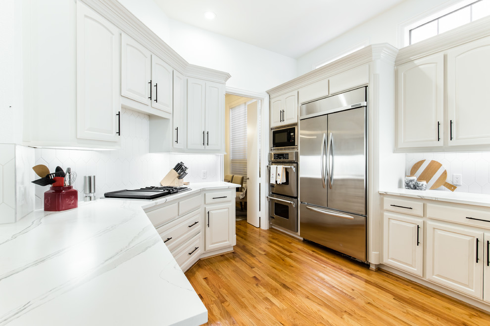 Example of a large classic galley light wood floor kitchen design in Dallas with white cabinets, quartz countertops, white backsplash, ceramic backsplash, stainless steel appliances, white countertops and shaker cabinets