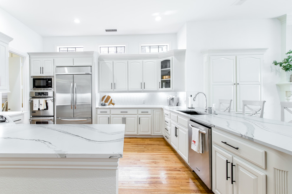 Inspiration for a large timeless galley light wood floor kitchen remodel in Dallas with white cabinets, quartz countertops, white backsplash, ceramic backsplash, stainless steel appliances and white countertops