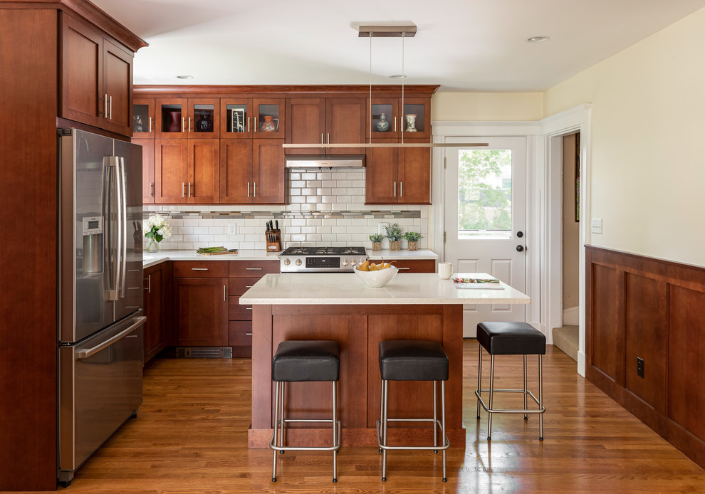 Exempel på ett mellanstort amerikanskt vit vitt l-kök, med en undermonterad diskho, skåp i shakerstil, skåp i mellenmörkt trä, bänkskiva i kvarts, vitt stänkskydd, stänkskydd i tunnelbanekakel, rostfria vitvaror, mellanmörkt trägolv, en köksö och brunt golv