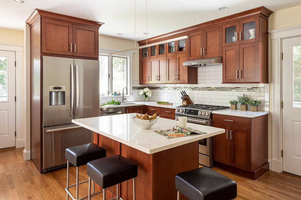 Mid-sized transitional l-shaped medium tone wood floor and brown floor kitchen photo in Boston with an undermount sink, shaker cabinets, medium tone wood cabinets, quartz countertops, white backsplash, subway tile backsplash, stainless steel appliances, an island and white countertops