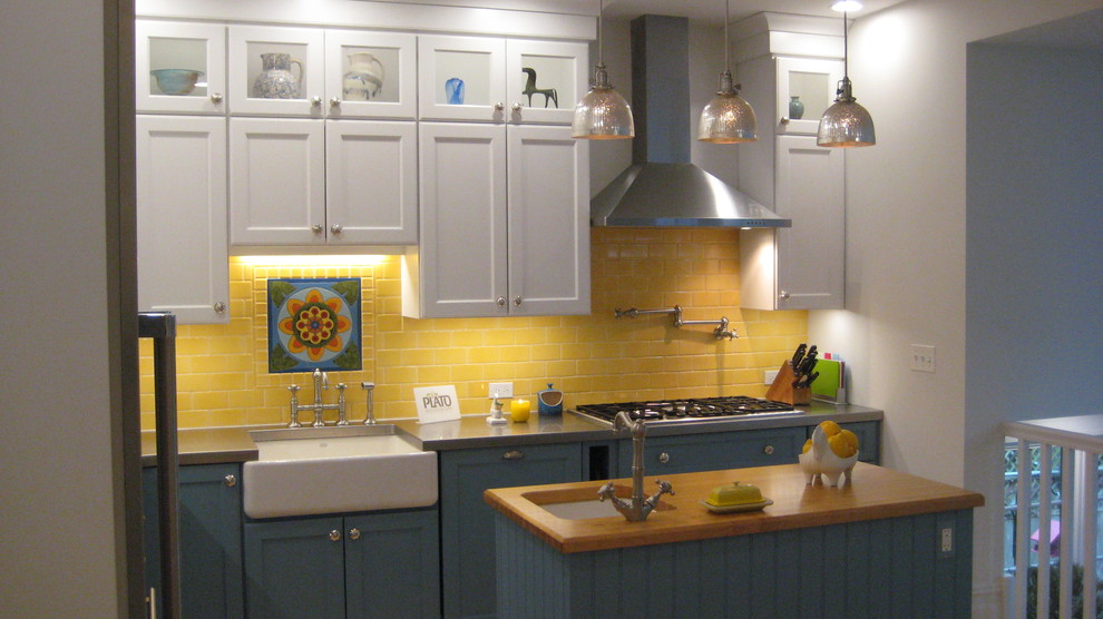 Inspiration for a rural l-shaped enclosed kitchen in Chicago with a belfast sink, shaker cabinets, white cabinets, wood worktops, yellow splashback, metro tiled splashback, stainless steel appliances and an island.