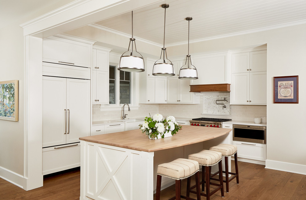 Inredning av ett klassiskt vit vitt kök, med en rustik diskho, skåp i shakerstil, vita skåp, bänkskiva i kvarts, beige stänkskydd, stänkskydd i keramik, integrerade vitvaror, mellanmörkt trägolv, en köksö och brunt golv