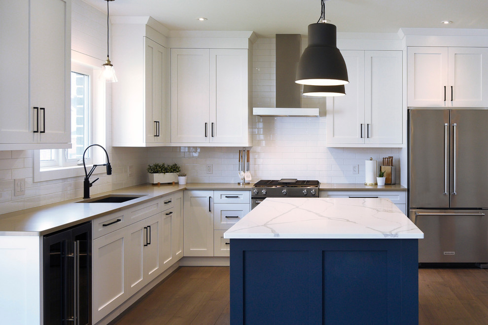 Large traditional l-shaped kitchen/diner in Toronto with recessed-panel cabinets, white cabinets, an island, a double-bowl sink, quartz worktops, white splashback, metro tiled splashback, stainless steel appliances and medium hardwood flooring.