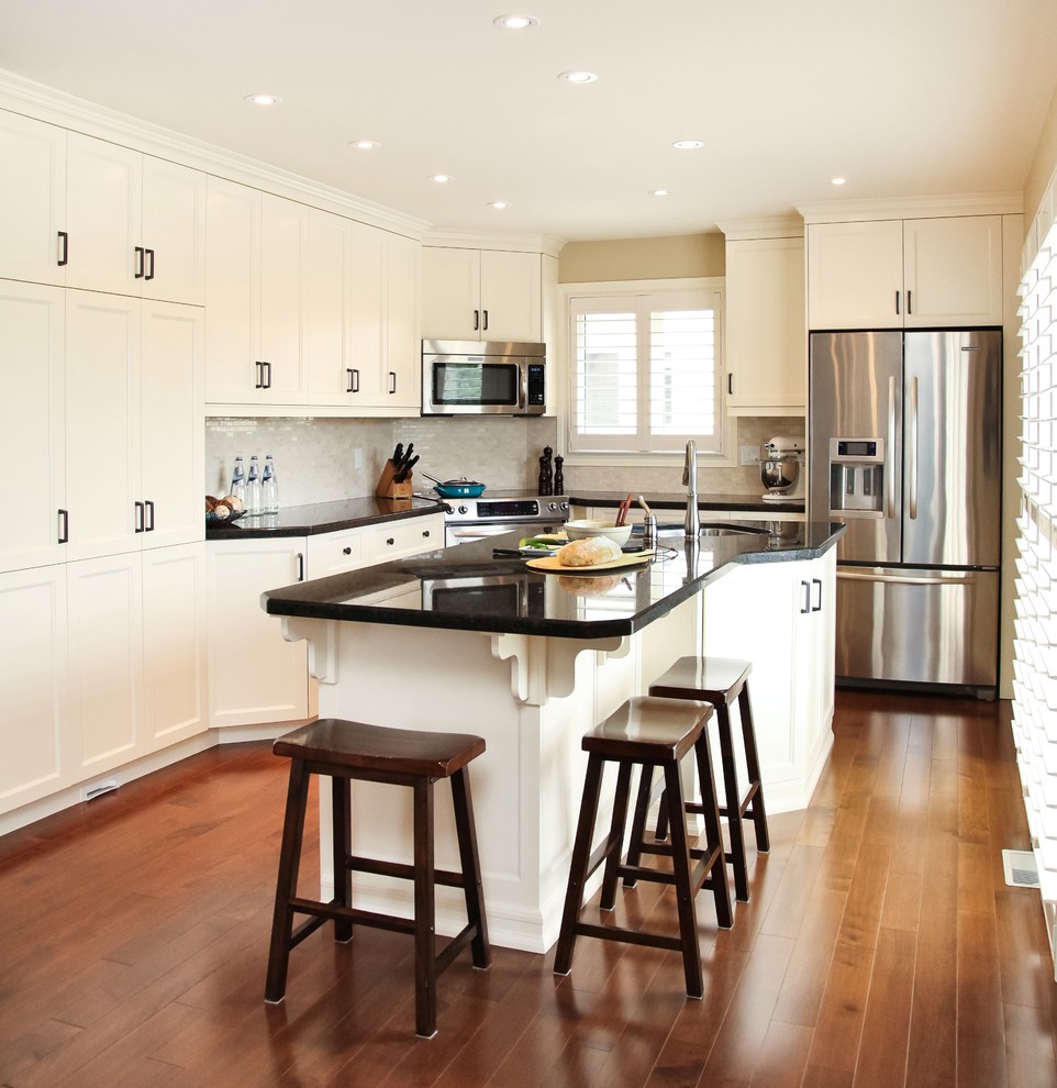 Large transitional l-shaped medium tone wood floor eat-in kitchen photo in Toronto with recessed-panel cabinets, white cabinets, beige backsplash, stainless steel appliances, granite countertops, stone tile backsplash, an island and an undermount sink