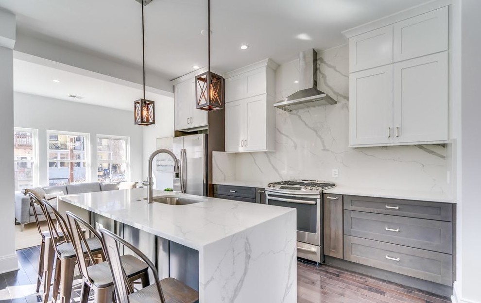 Design ideas for a classic galley open plan kitchen in DC Metro with a submerged sink, shaker cabinets, white cabinets, white splashback, stainless steel appliances, dark hardwood flooring, an island, brown floors and white worktops.