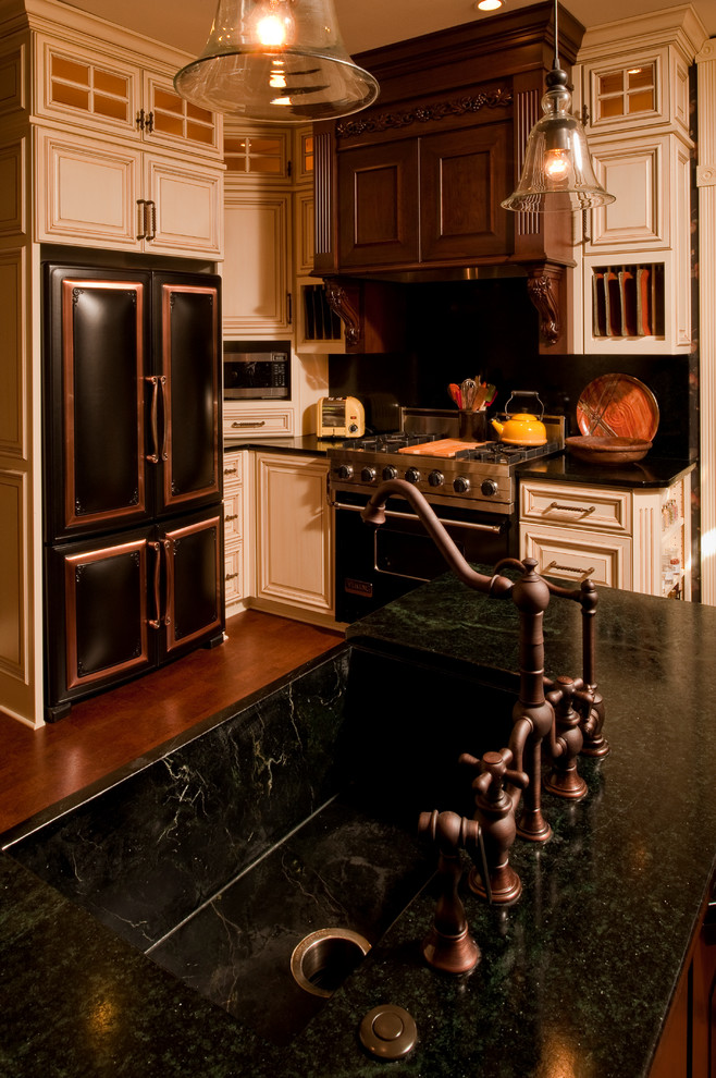 Exempel på ett mellanstort, avskilt klassiskt l-kök, med en rustik diskho, luckor med upphöjd panel, skåp i slitet trä, bänkskiva i kvartsit, svart stänkskydd, stänkskydd i sten, svarta vitvaror, mörkt trägolv, en köksö och brunt golv