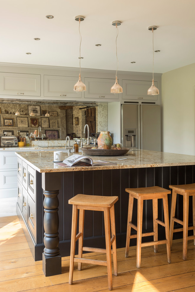 Cette image montre une cuisine américaine bohème avec un placard à porte shaker, des portes de placard grises, une crédence miroir, un sol en bois brun et îlot.