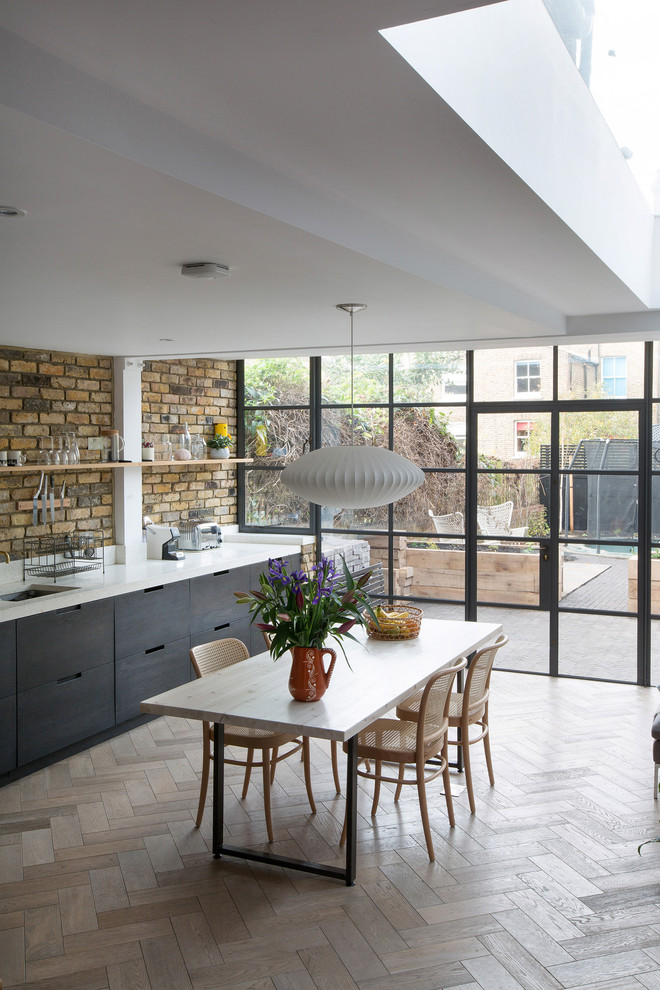 Inspiration for a large contemporary single-wall open plan kitchen in London with a single-bowl sink, flat-panel cabinets, black cabinets, composite countertops, white splashback, medium hardwood flooring and brown floors.