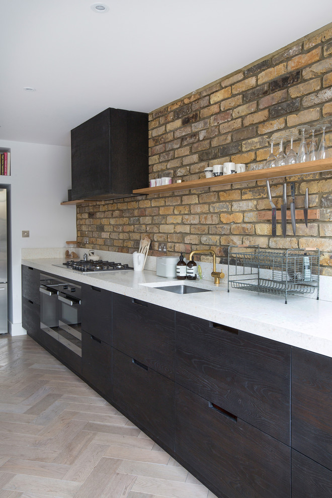Exemple d'une grande cuisine ouverte linéaire tendance avec un placard à porte plane, des portes de placard noires, un plan de travail en surface solide, une crédence blanche, un sol en bois brun, un sol marron et un évier intégré.