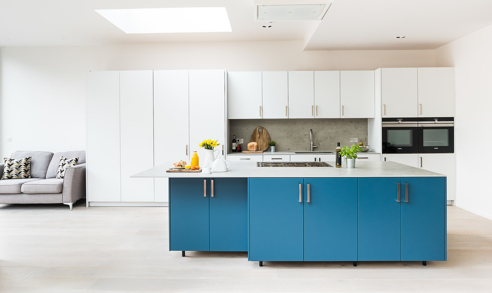 Inspiration for a large contemporary kitchen in London with an integrated sink, flat-panel cabinets, turquoise cabinets, concrete worktops, grey splashback, slate splashback, stainless steel appliances, light hardwood flooring, an island and grey floors.