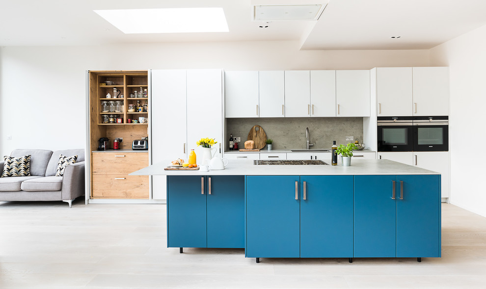 Photo of a large contemporary galley open plan kitchen in London with an integrated sink, flat-panel cabinets, turquoise cabinets, concrete worktops, grey splashback, slate splashback, stainless steel appliances, light hardwood flooring, an island, grey floors and grey worktops.
