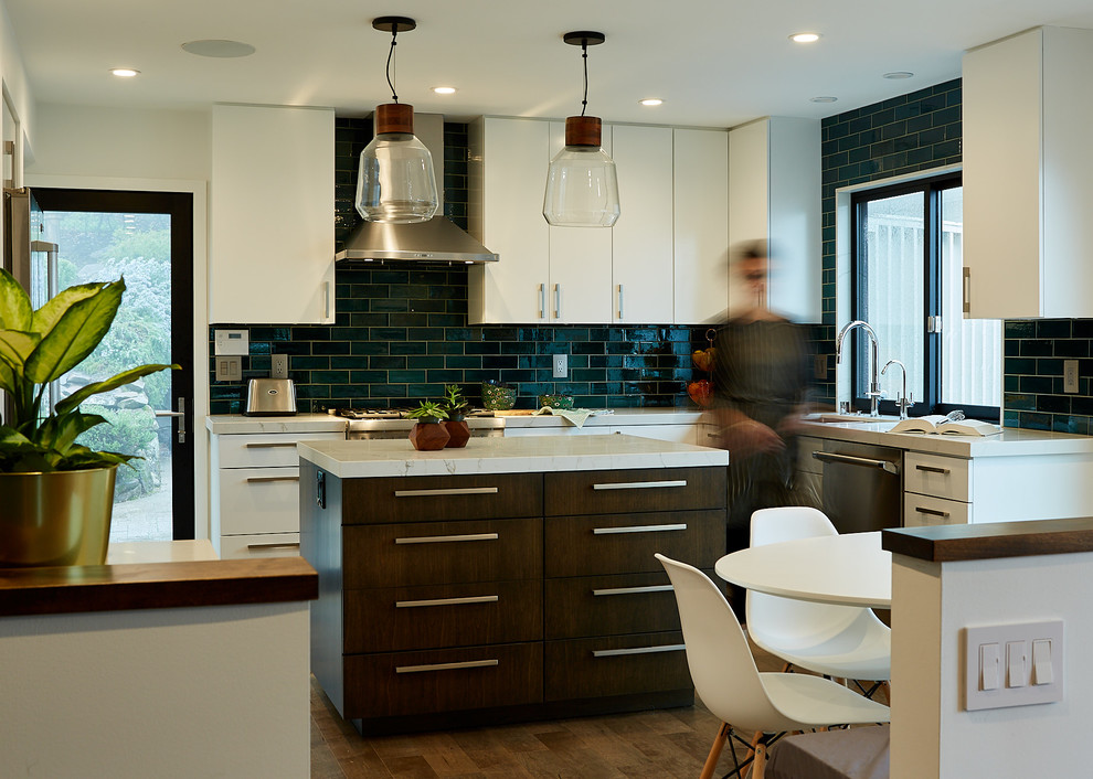 This is an example of a medium sized contemporary l-shaped kitchen/diner in San Francisco with a submerged sink, flat-panel cabinets, white cabinets, blue splashback, metro tiled splashback, stainless steel appliances, medium hardwood flooring, an island, brown floors, white worktops and engineered stone countertops.