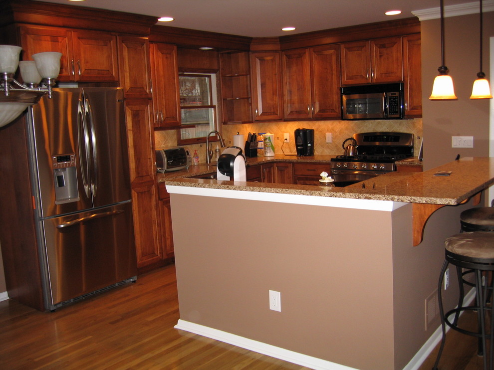 Example of a large transitional l-shaped medium tone wood floor eat-in kitchen design in New York with an undermount sink, raised-panel cabinets, medium tone wood cabinets, quartz countertops, beige backsplash, porcelain backsplash, stainless steel appliances and an island