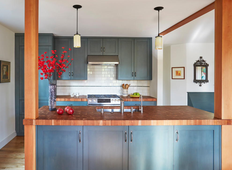 Inspiration for a mid-sized craftsman single-wall medium tone wood floor and brown floor open concept kitchen remodel in San Francisco with an undermount sink, shaker cabinets, blue cabinets, wood countertops, white backsplash, porcelain backsplash, paneled appliances, an island and brown countertops
