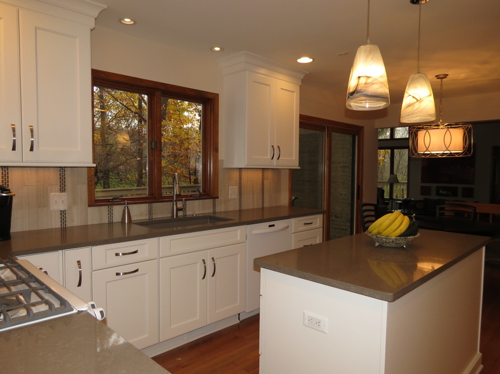 This is an example of a medium sized modern kitchen/diner in Detroit with a submerged sink, flat-panel cabinets, white cabinets, grey splashback, stone tiled splashback, white appliances, medium hardwood flooring and an island.