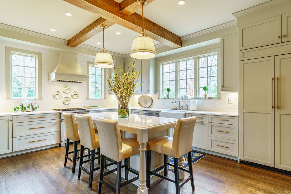 Foto de cocinas en L tradicional con fregadero sobremueble, armarios estilo shaker, puertas de armario beige, salpicadero blanco, electrodomésticos con paneles, suelo de madera en tonos medios, una isla, suelo marrón y encimeras blancas