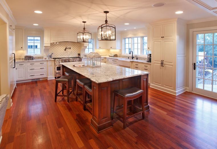 Example of a huge classic u-shaped medium tone wood floor eat-in kitchen design in Minneapolis with a farmhouse sink, raised-panel cabinets, white cabinets, granite countertops, white backsplash, porcelain backsplash, paneled appliances and an island