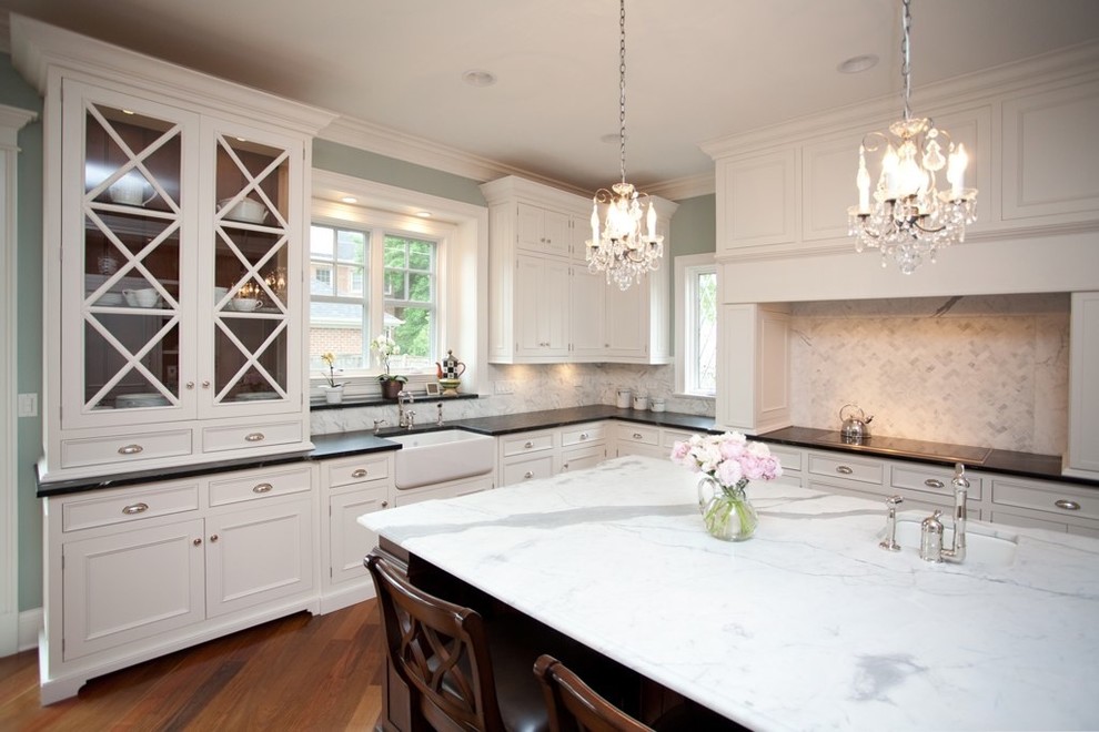 Inspiration for a large timeless u-shaped medium tone wood floor eat-in kitchen remodel in Chicago with recessed-panel cabinets, a farmhouse sink, marble countertops, white cabinets, white backsplash, stone tile backsplash, paneled appliances and an island