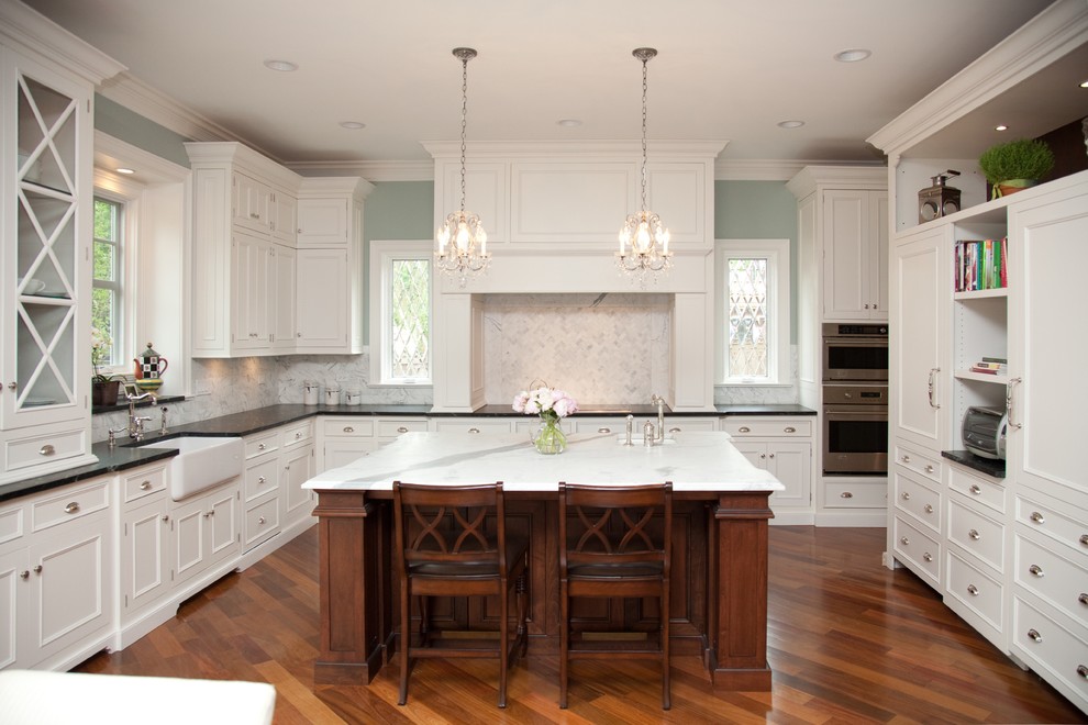 Elegant kitchen photo in Chicago with recessed-panel cabinets, a farmhouse sink, white backsplash and stone tile backsplash