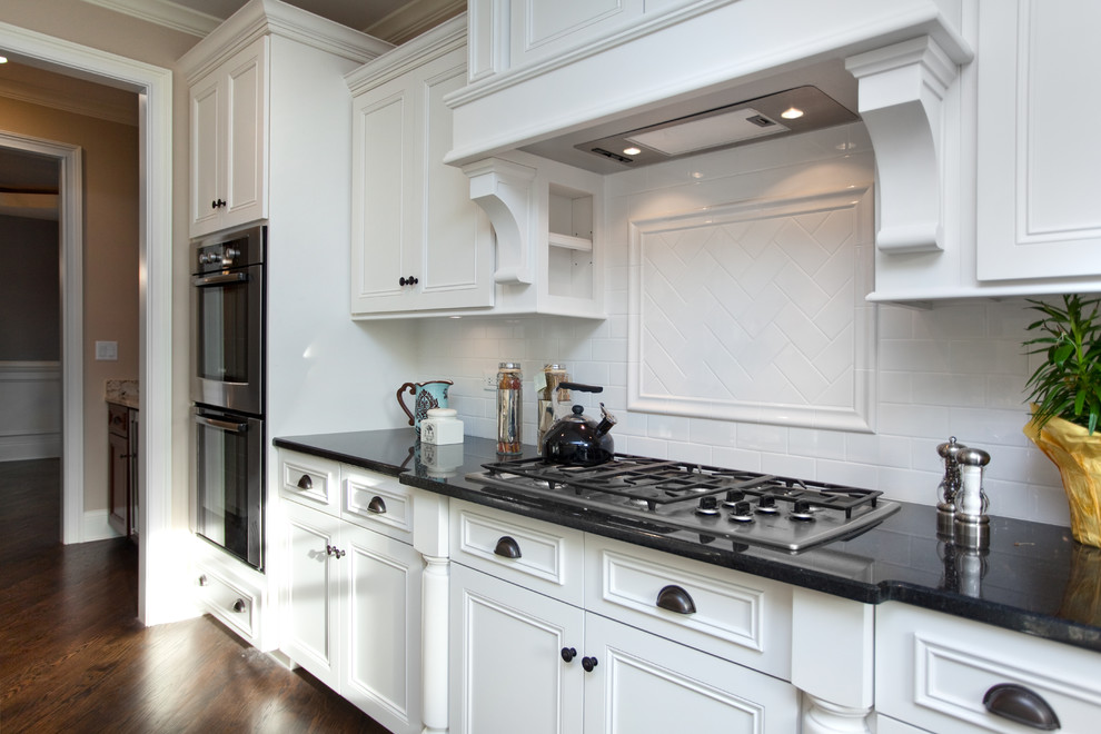 Design ideas for a large traditional l-shaped enclosed kitchen in Chicago with recessed-panel cabinets, white cabinets, granite worktops, white splashback, metro tiled splashback, stainless steel appliances and dark hardwood flooring.