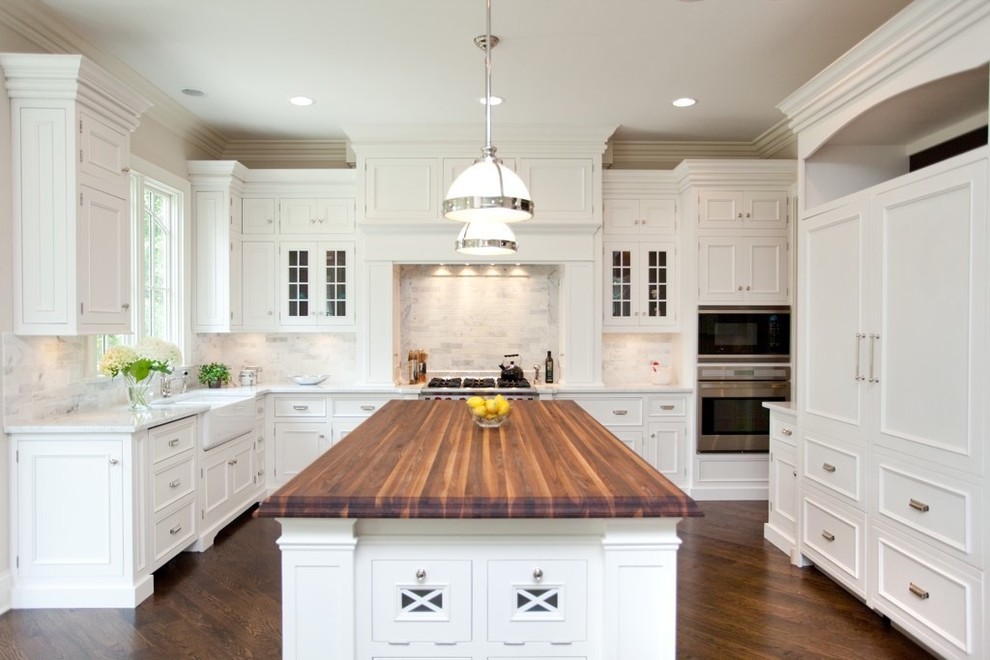 Enclosed kitchen - mid-sized traditional l-shaped dark wood floor enclosed kitchen idea in Chicago with recessed-panel cabinets, a farmhouse sink, wood countertops, white cabinets, white backsplash, stone tile backsplash, stainless steel appliances and an island